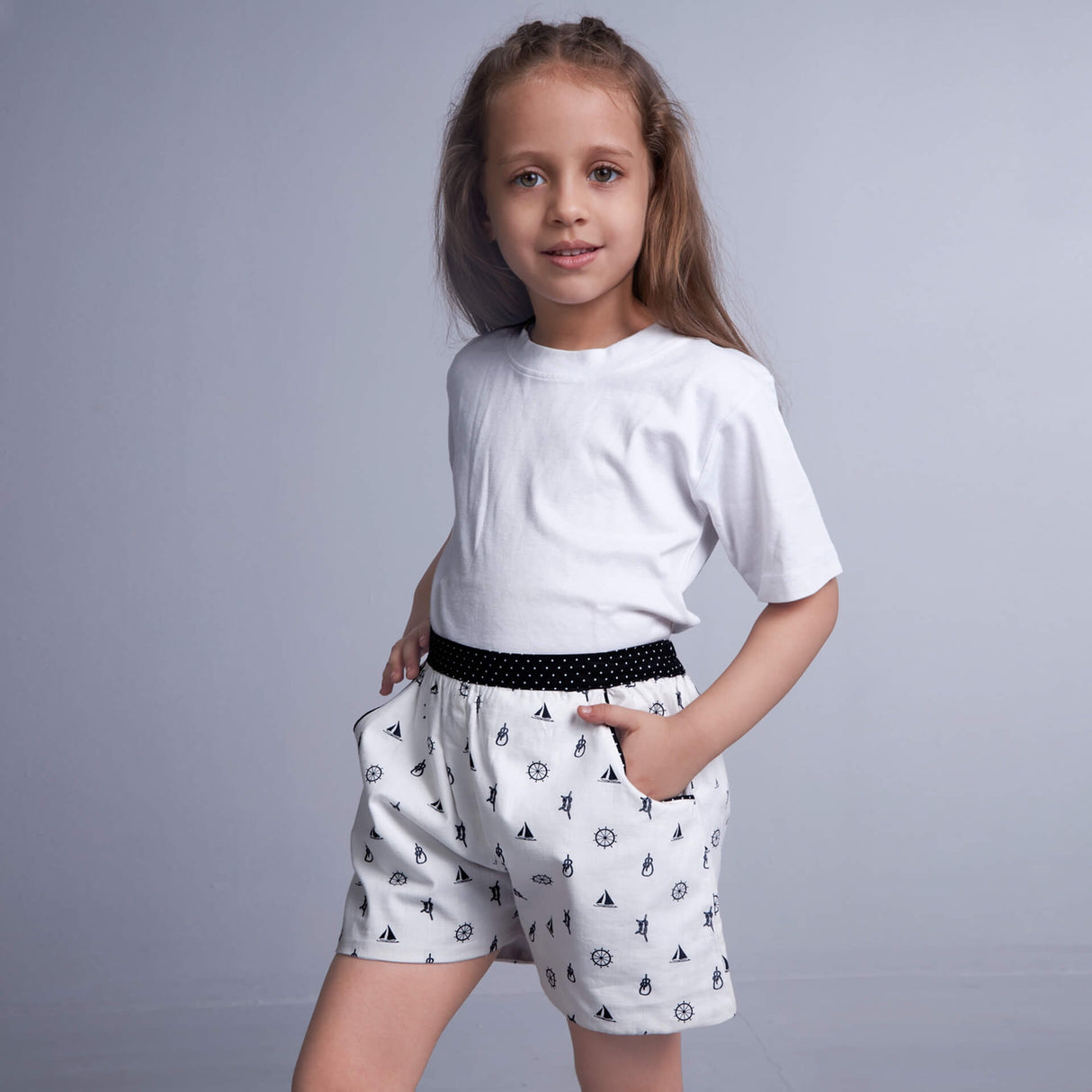 Side pose of a girl wearing white shorts in boats printed fabric, with her hands inserted into the pockets