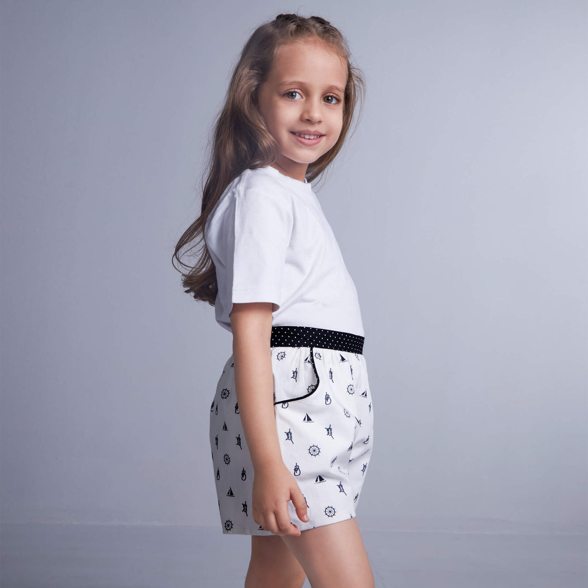 A girl wears white boat printed shorts featuring dual side pockets, elasticated waist, and black dotted fabric trims
