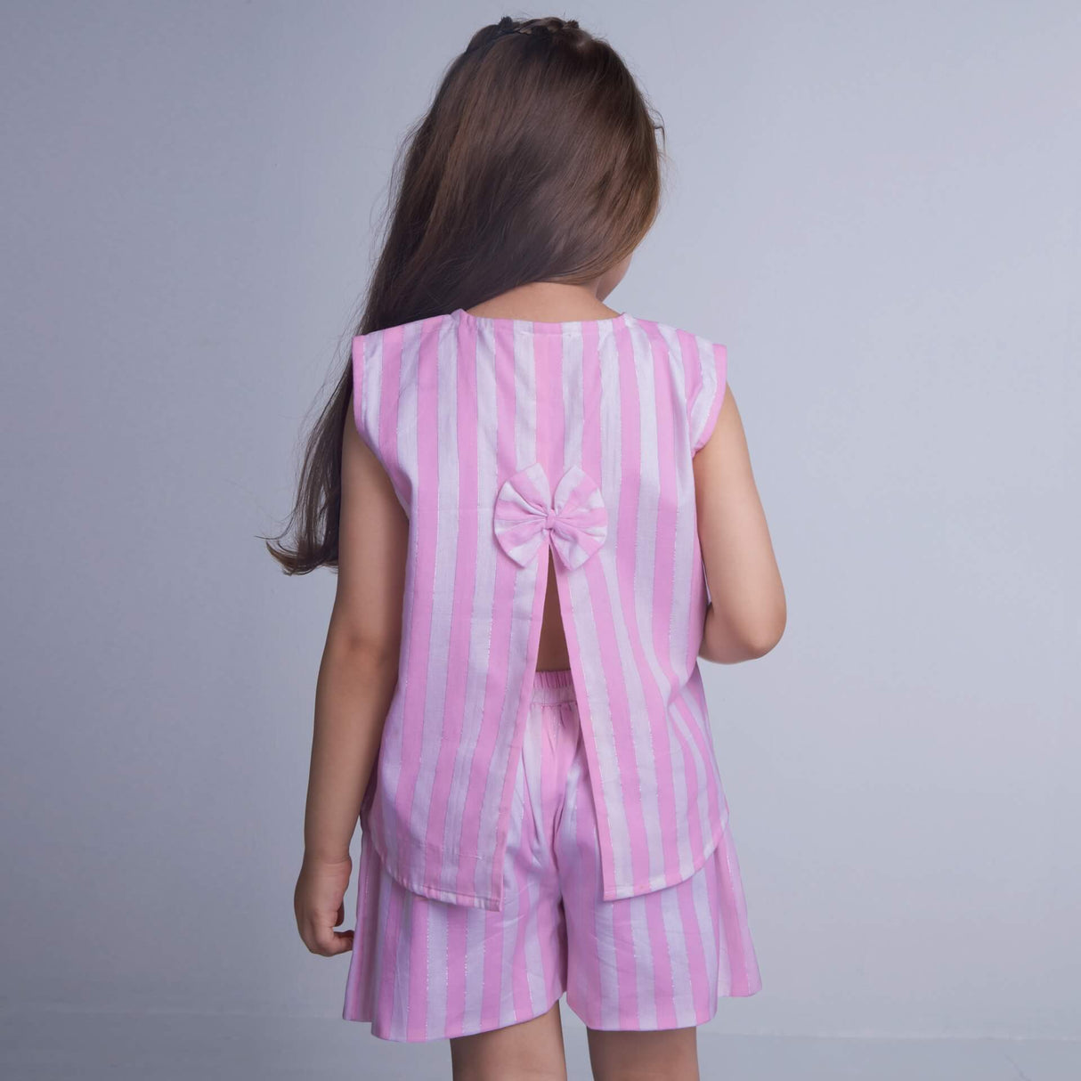 A girl is seen from the back, wearing a pink striped sleeveless blouse with a slit at the back, paired with shorts