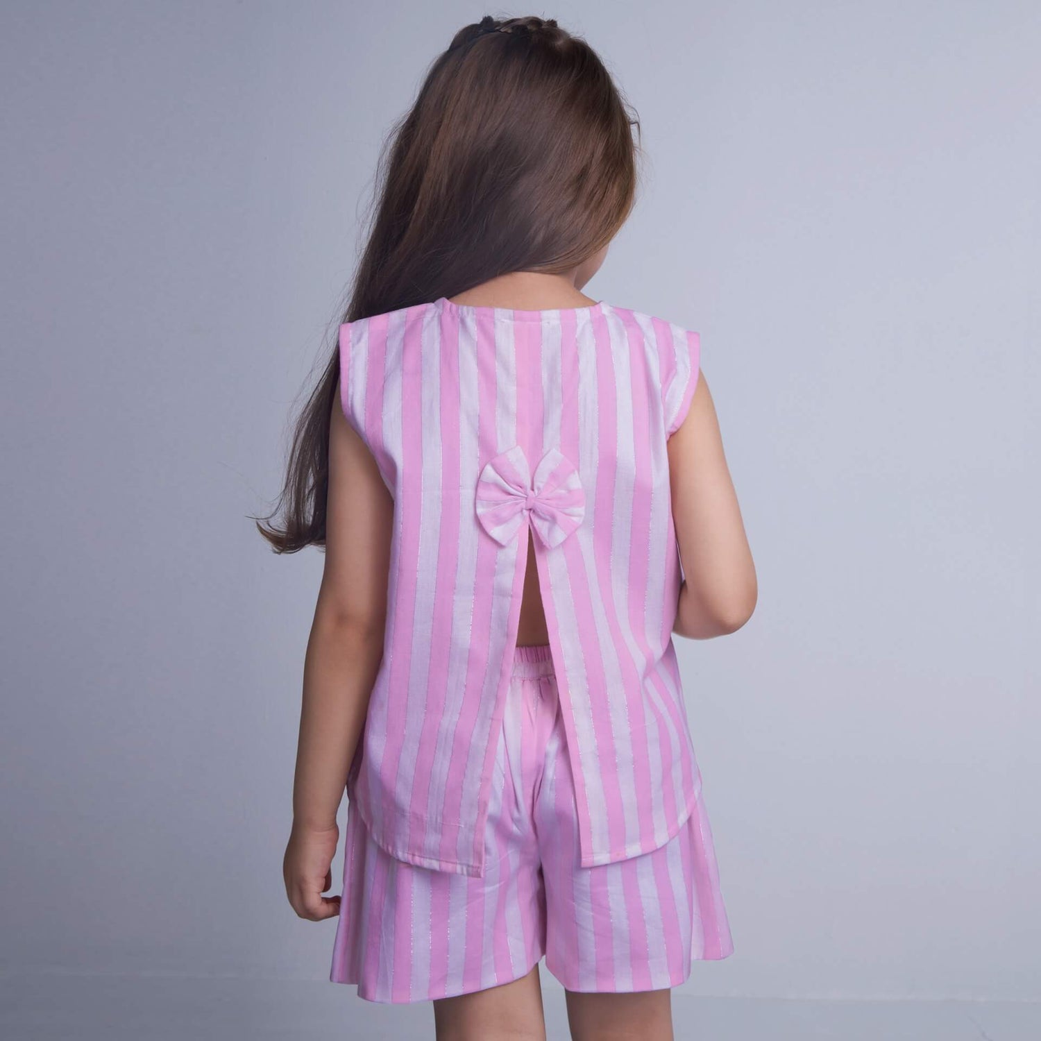 A girl is seen from the back, wearing a pink striped sleeveless blouse with a slit at the back, paired with shorts