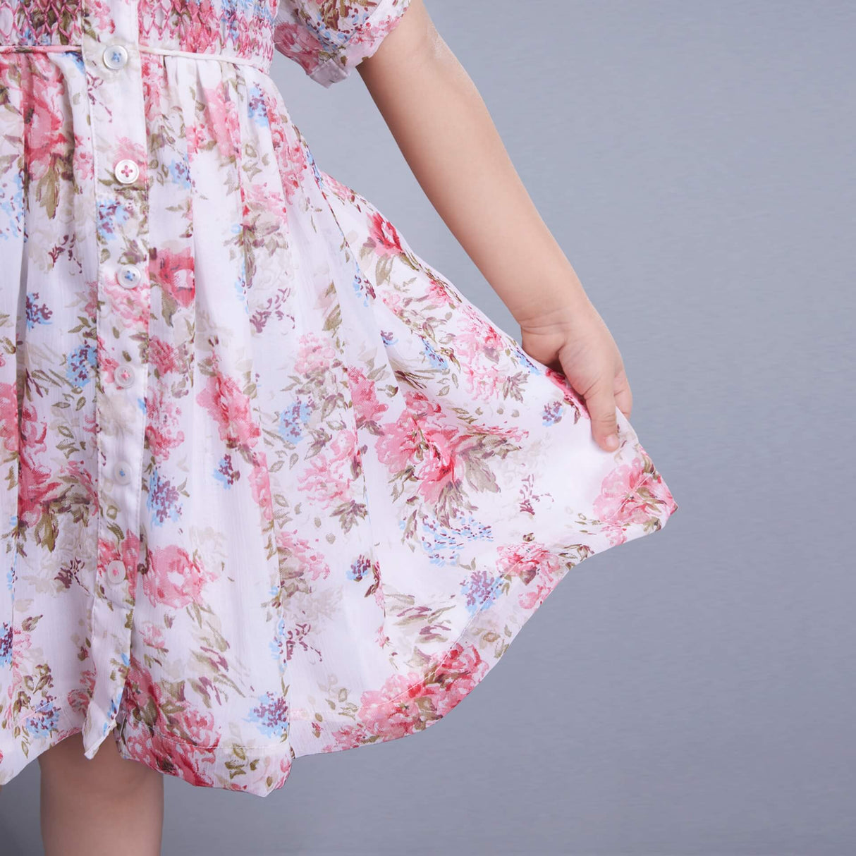 Detailed close-up of an ivory chiffon smocked dress with decorative buttons fastened at the front