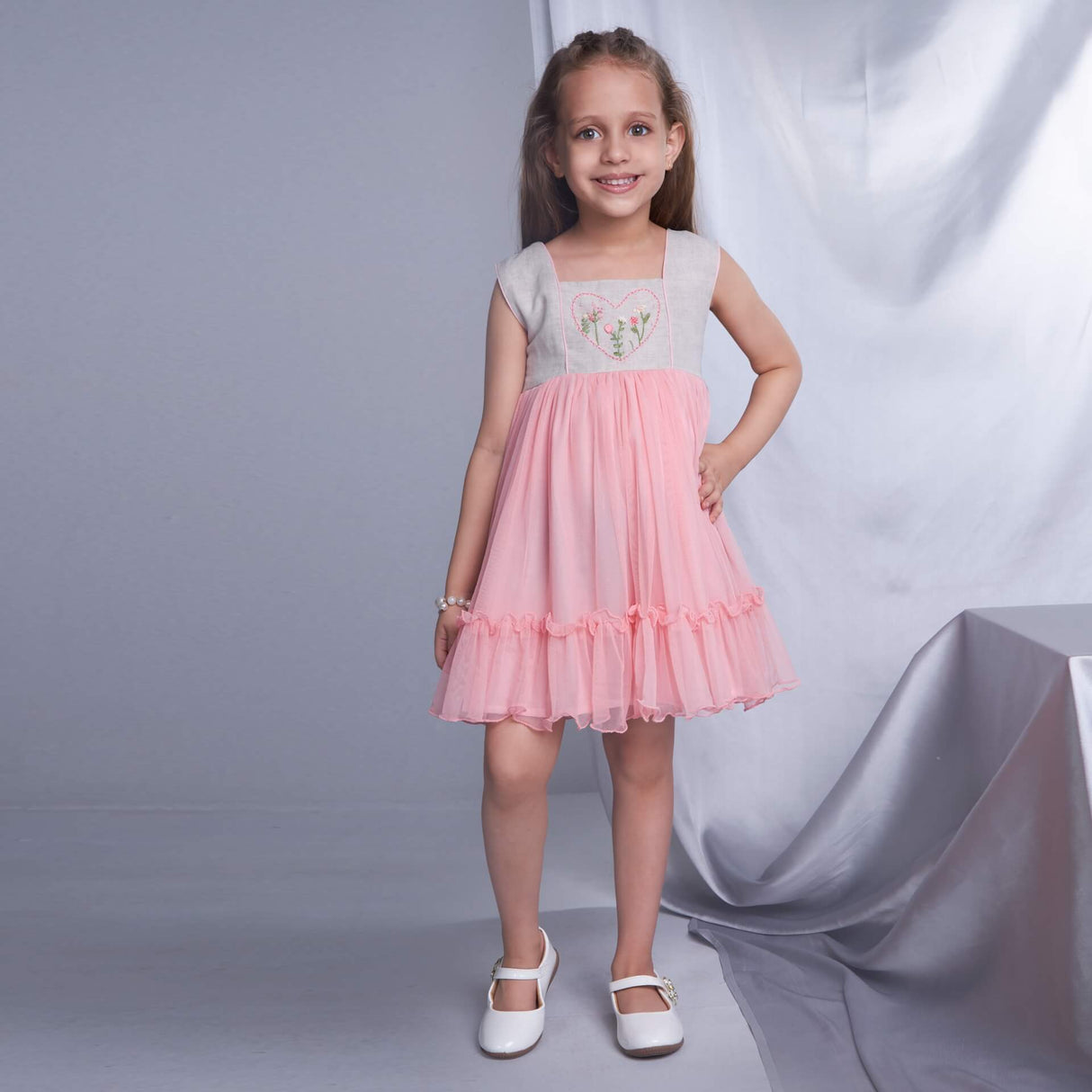 A smiling girl wearing a peach dress with a heart hand embroidered yoke and hem ruffles