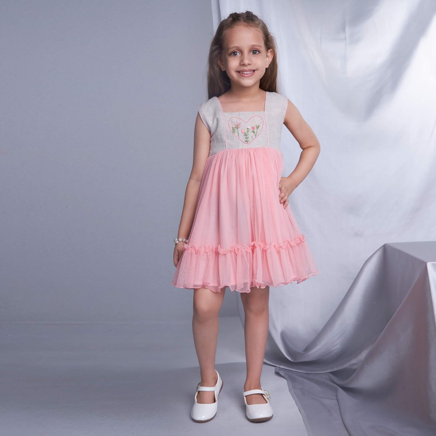 A smiling girl wearing a peach dress with a heart hand embroidered yoke and hem ruffles