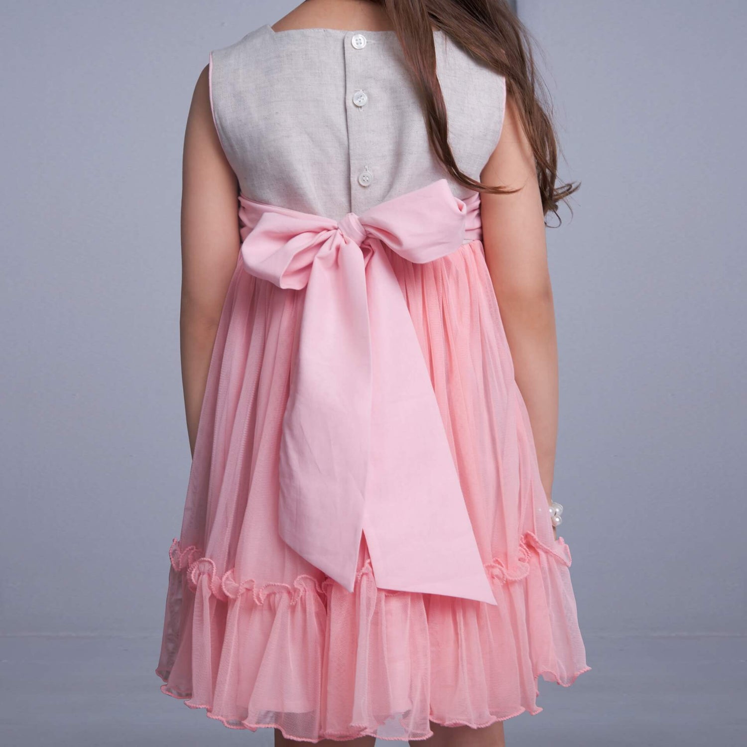 Girl seen from behind wearing a peach hand-embroidered tulle dress with a tie-up sash at the back