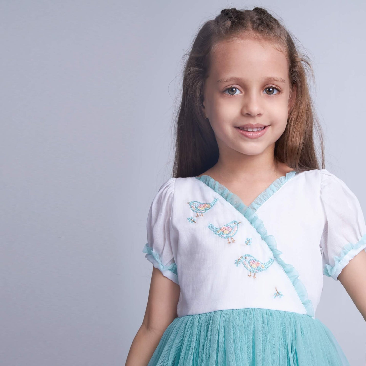 Close-up view of the delicate pastel bird embroidery on an aqua crossover tulle dress, featuring a V-shaped ruffled neckline