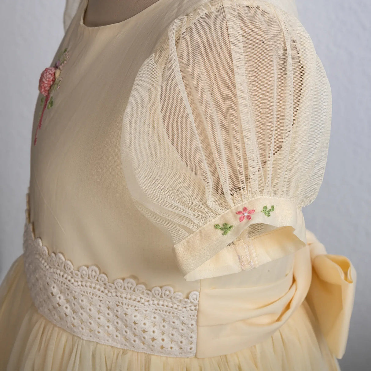 "Close-up of the floral hand embroidery on the puff sleeve of a yellow tulle dress."