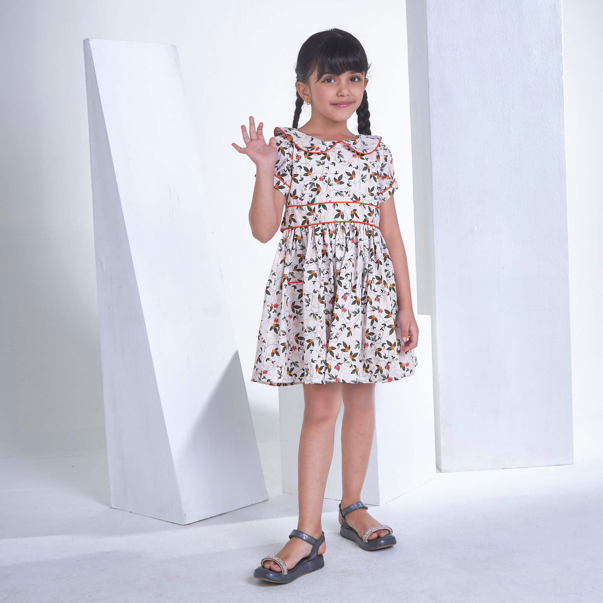 A girl posing with a wave, dressed in an ivory floral printed collared dress with an adjustable belt