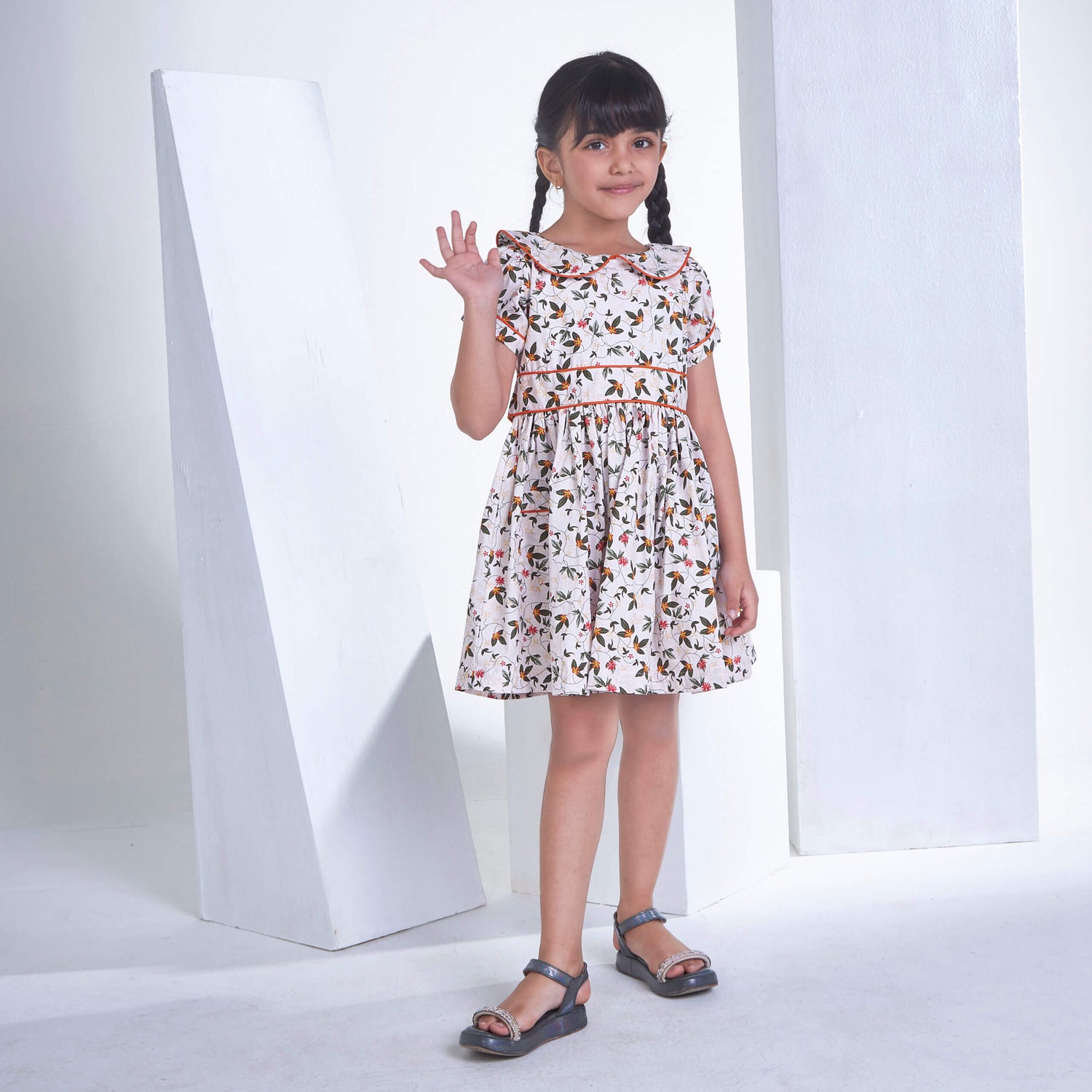 A girl posing with a wave, dressed in an ivory floral printed collared dress with an adjustable belt