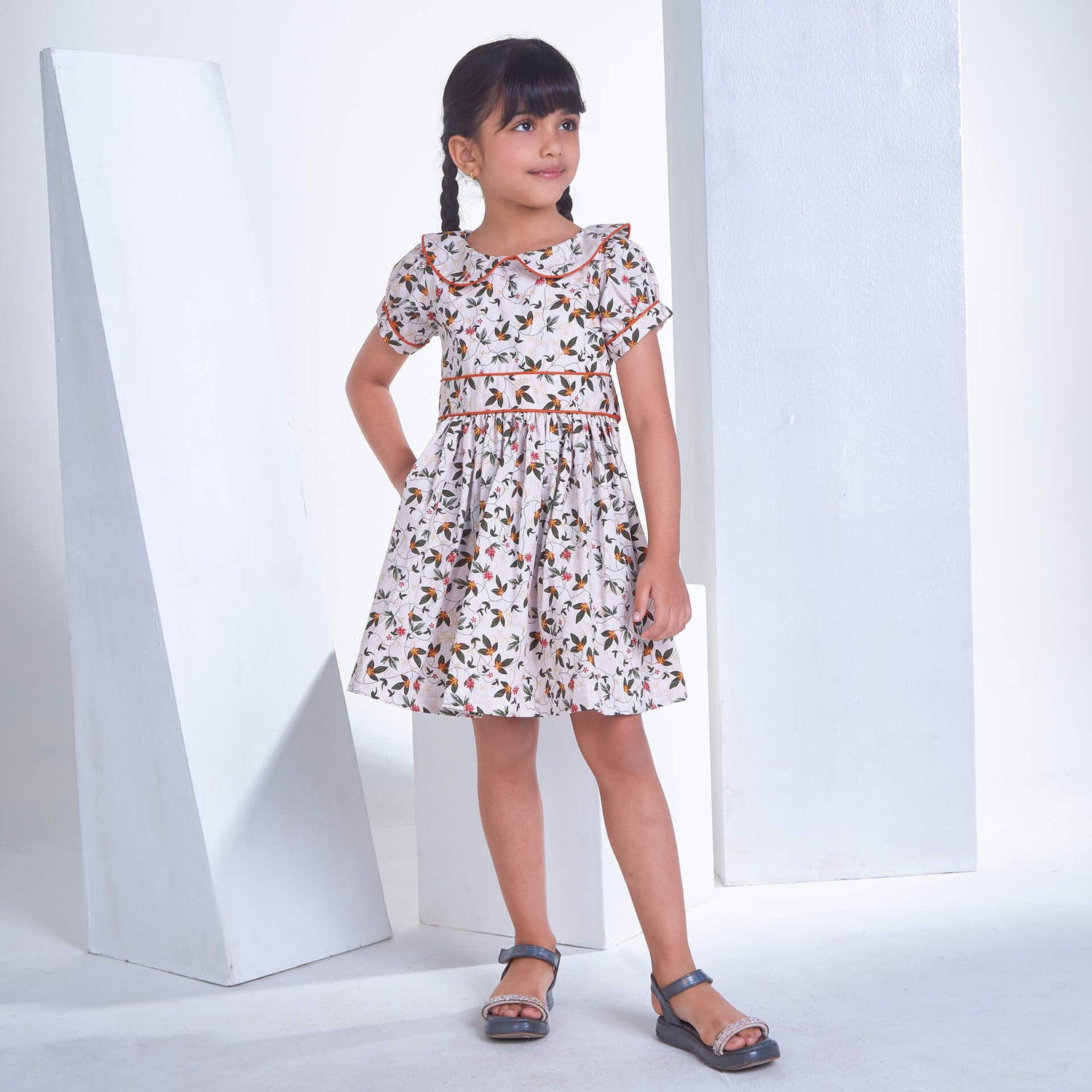A girl stands in an ivory floral printed collared dress with an adjustable belt at the waist