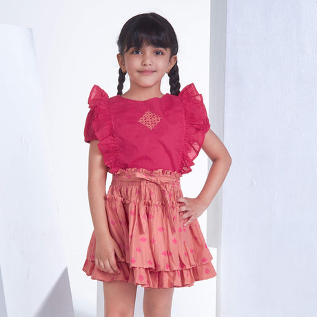 A girl in pink embroidered ruffle blouse and peach floral printed high waist skirt