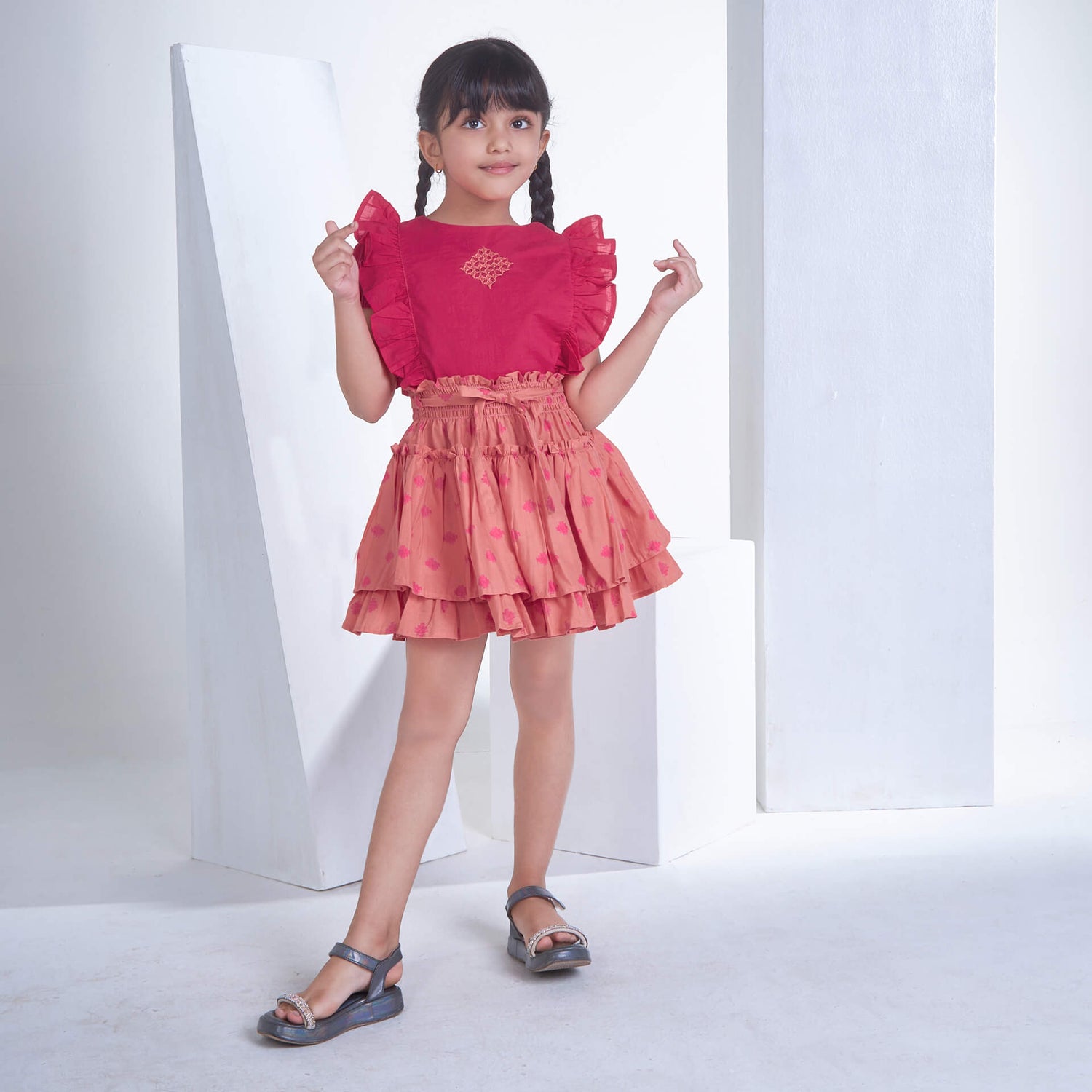 A little girl in pink embroidered ruffle blouse and peach floral printed high waist skirt