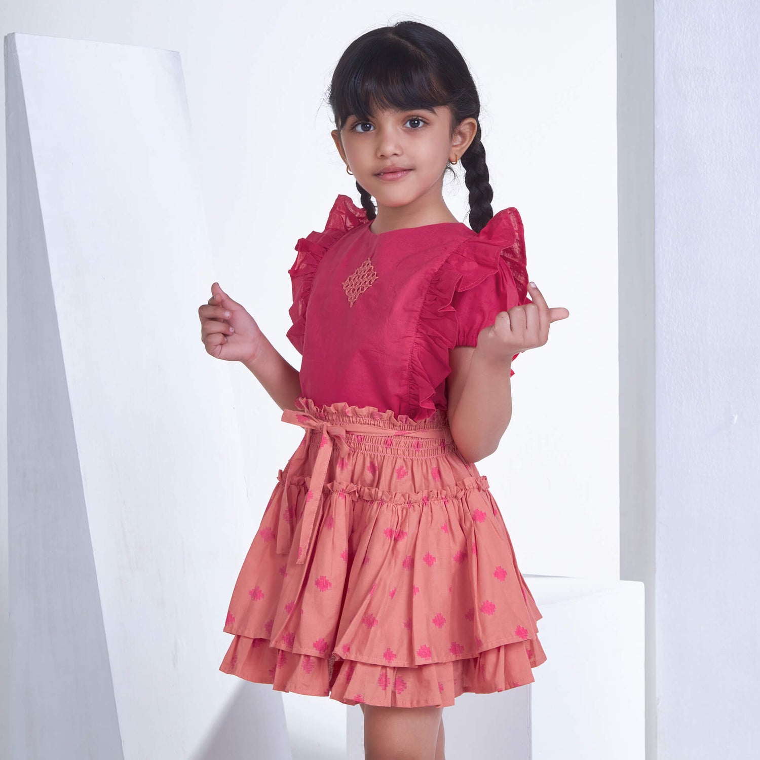 From the side, a girl dressed in pink embroidered ruffle blouse and peach floral printed high waist skirt