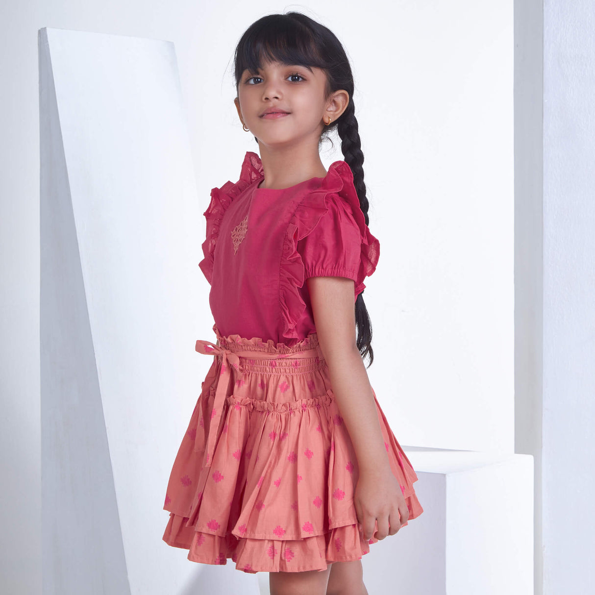 From the side, a girl dressed in pink embroidered ruffle blouse and peach floral printed high waist skirt