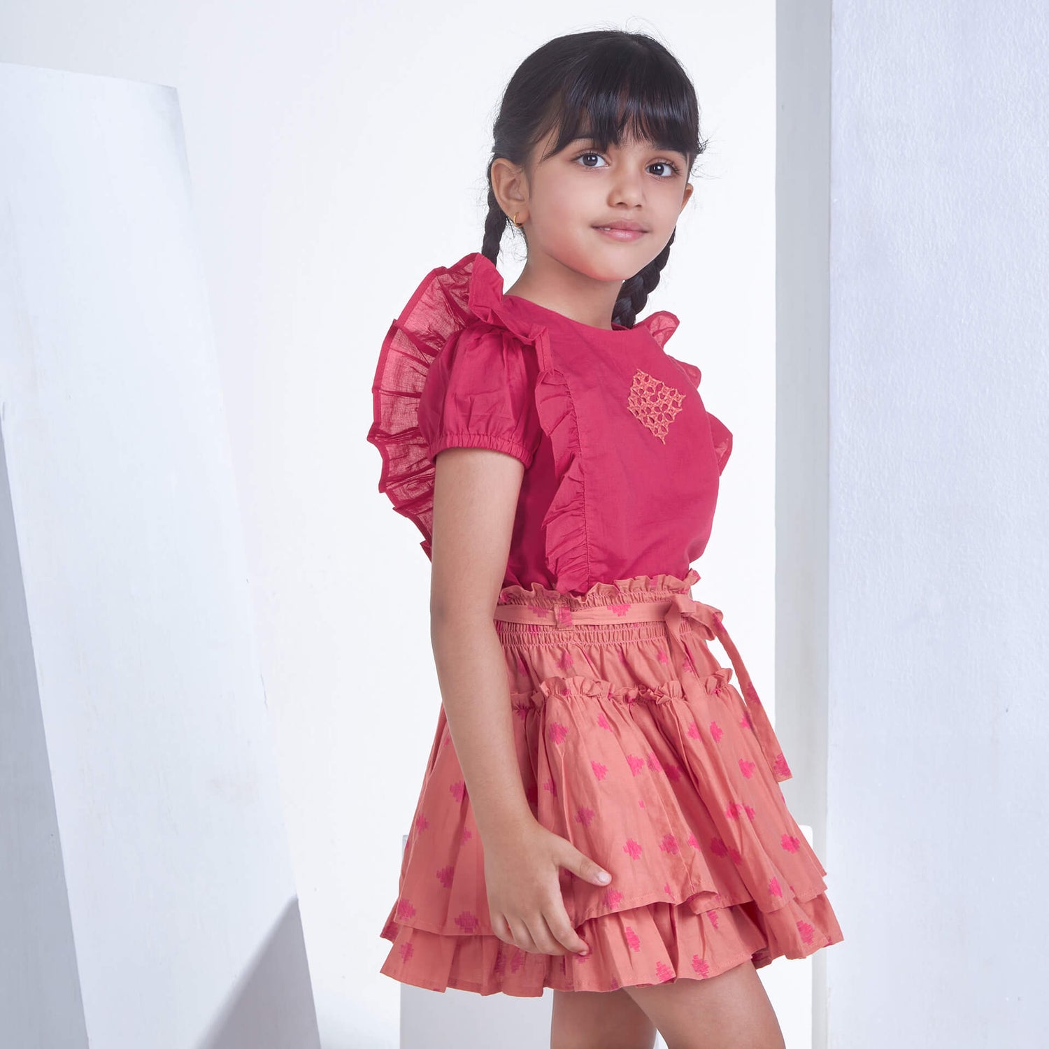 Side pose of a girl in pink embroidered ruffle blouse and peach floral printed high waist skirt