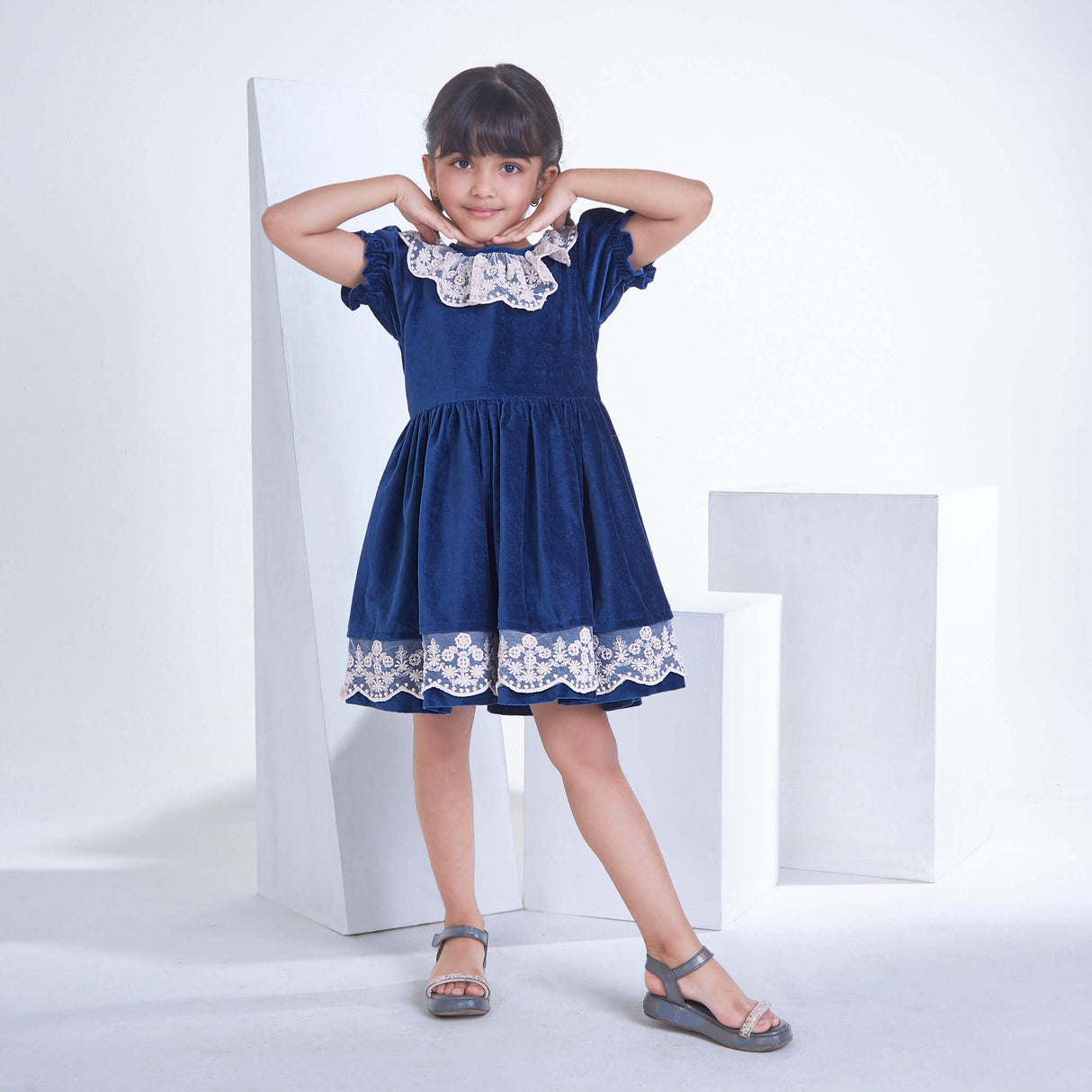 A little girl dressed in Navy velvet dress adorned with white lace, with a smiling pose