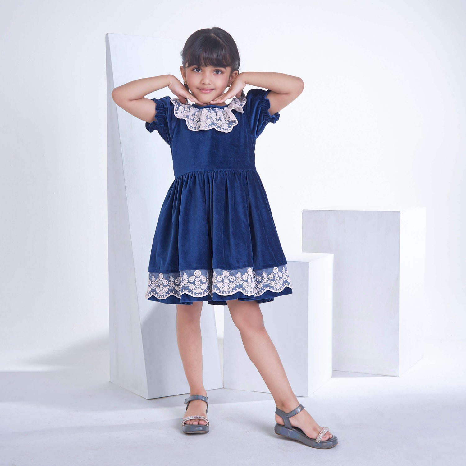 A little girl dressed in Navy velvet dress adorned with white lace, with a smiling pose