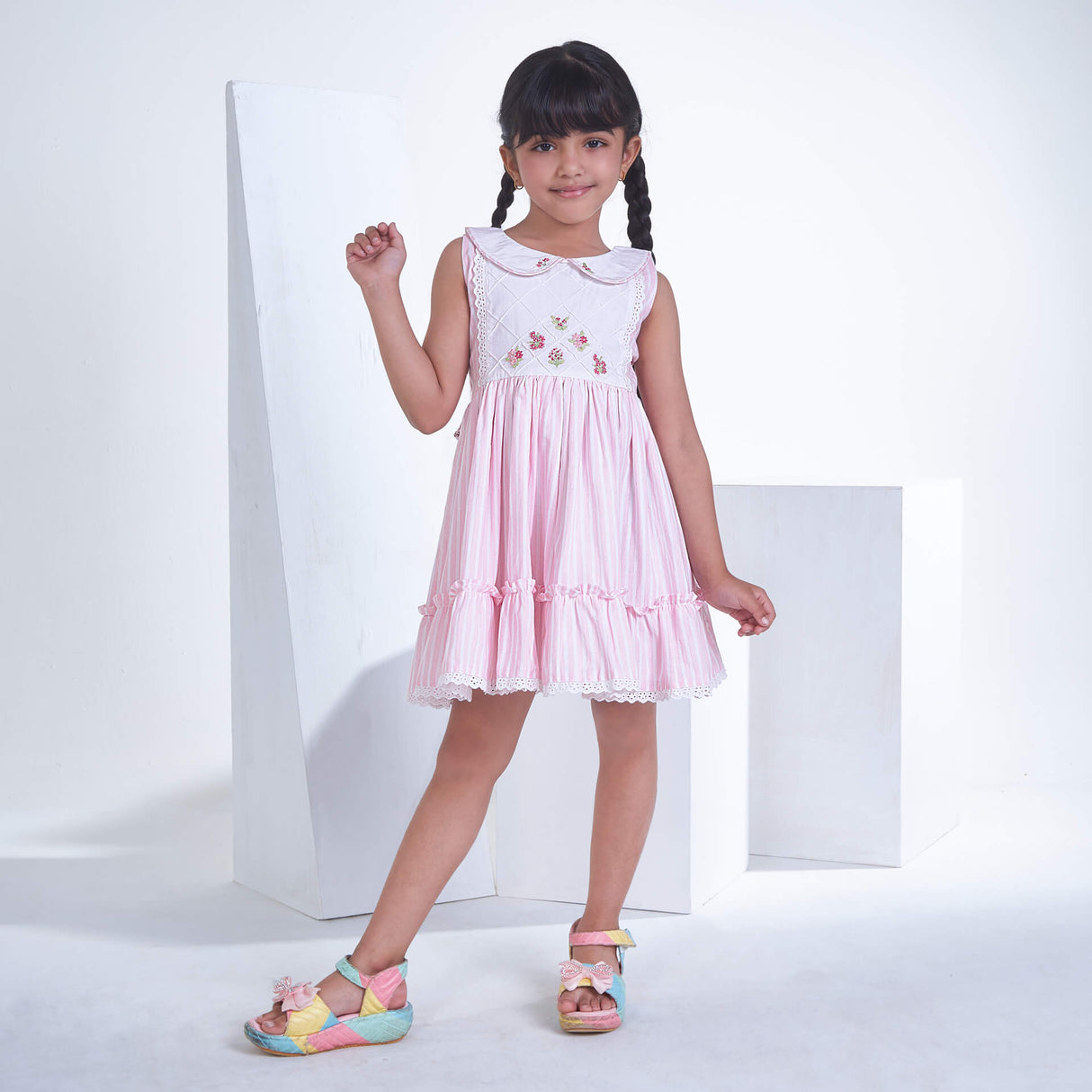 A little girl posing in pink striped embroidered collared dress adorned with ruffled hem