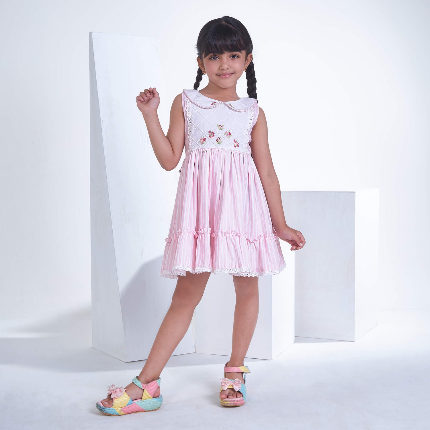 A little girl posing in pink striped embroidered collared dress adorned with ruffled hem