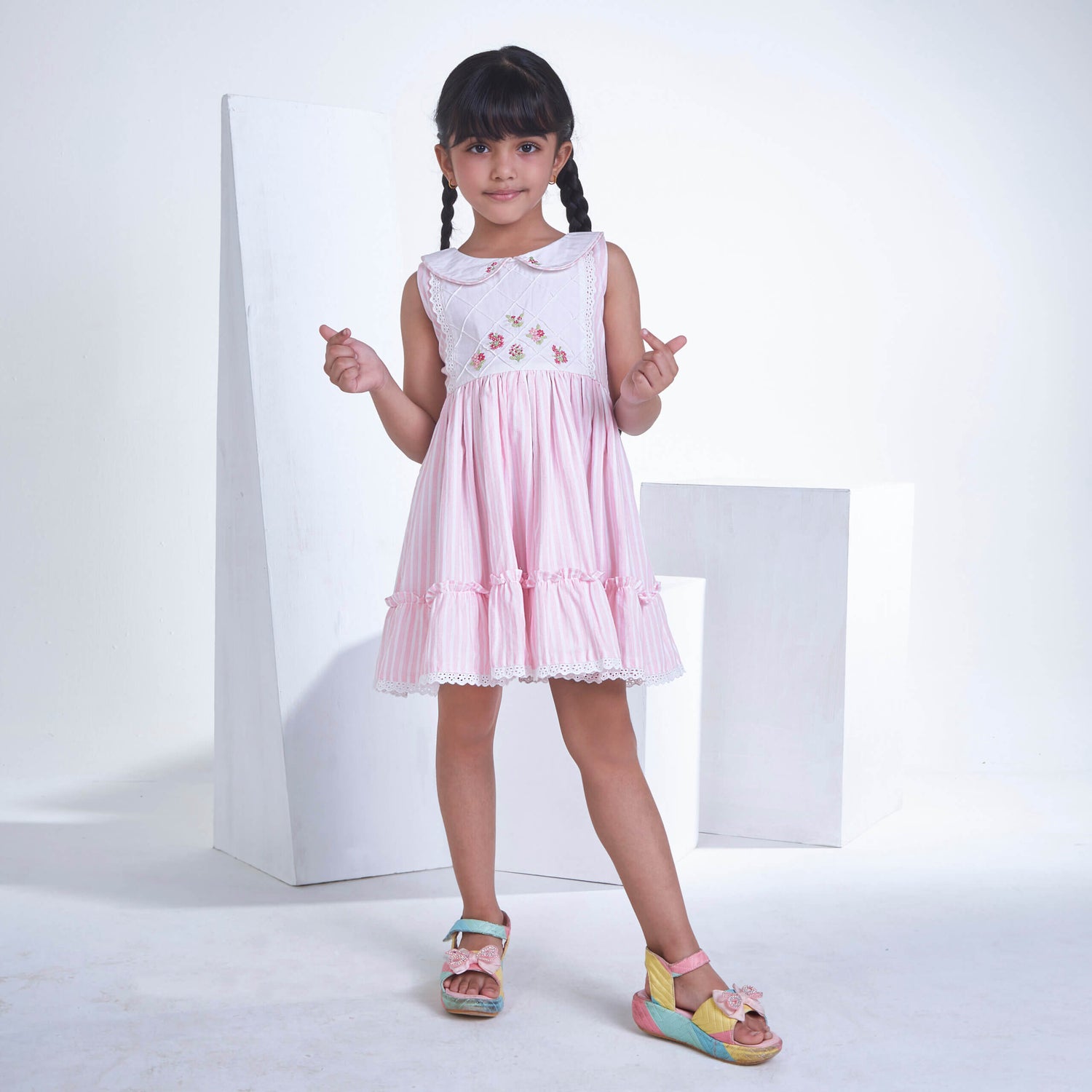 Smiling girl dressed in pink striped embroidered collared dress adorned with ruffled hem