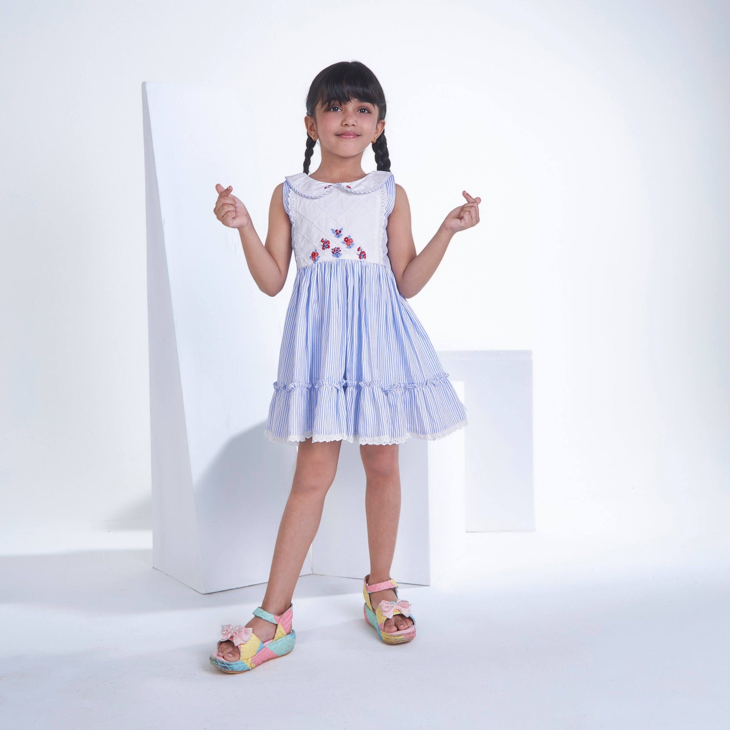 A little girl posing in blue striped embroidered collared dress adorned with ruffled hem