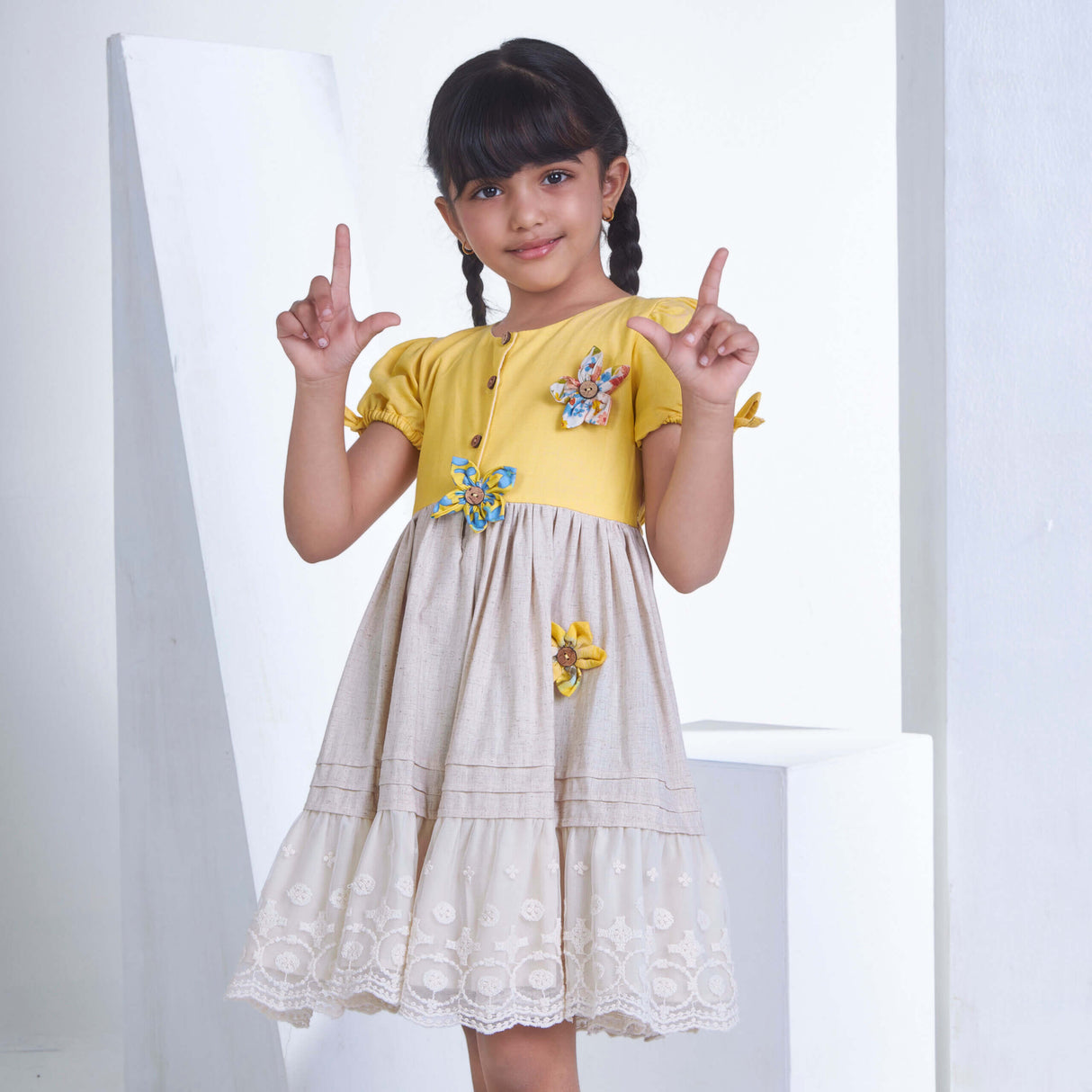 With a cute pose, a little one wears a yellow flower applique dress adorned with lace