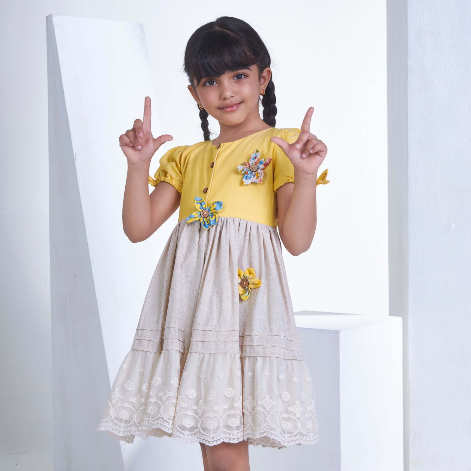 With a cute pose, a little one wears a yellow flower applique dress adorned with lace