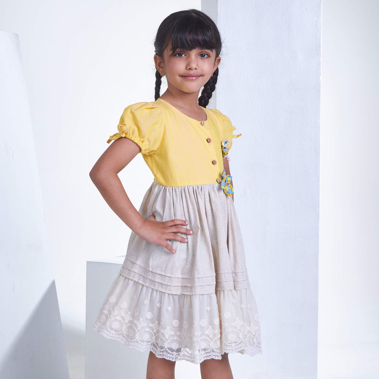 With hand on hips, a little girl stands in a yellow flower applique dress