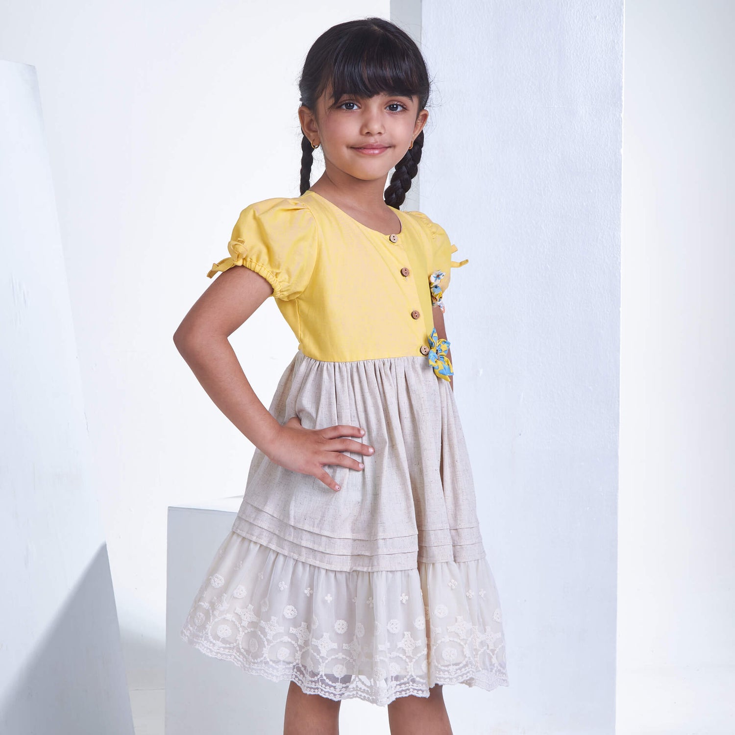 With hand on hips, a little girl stands in a yellow flower applique dress