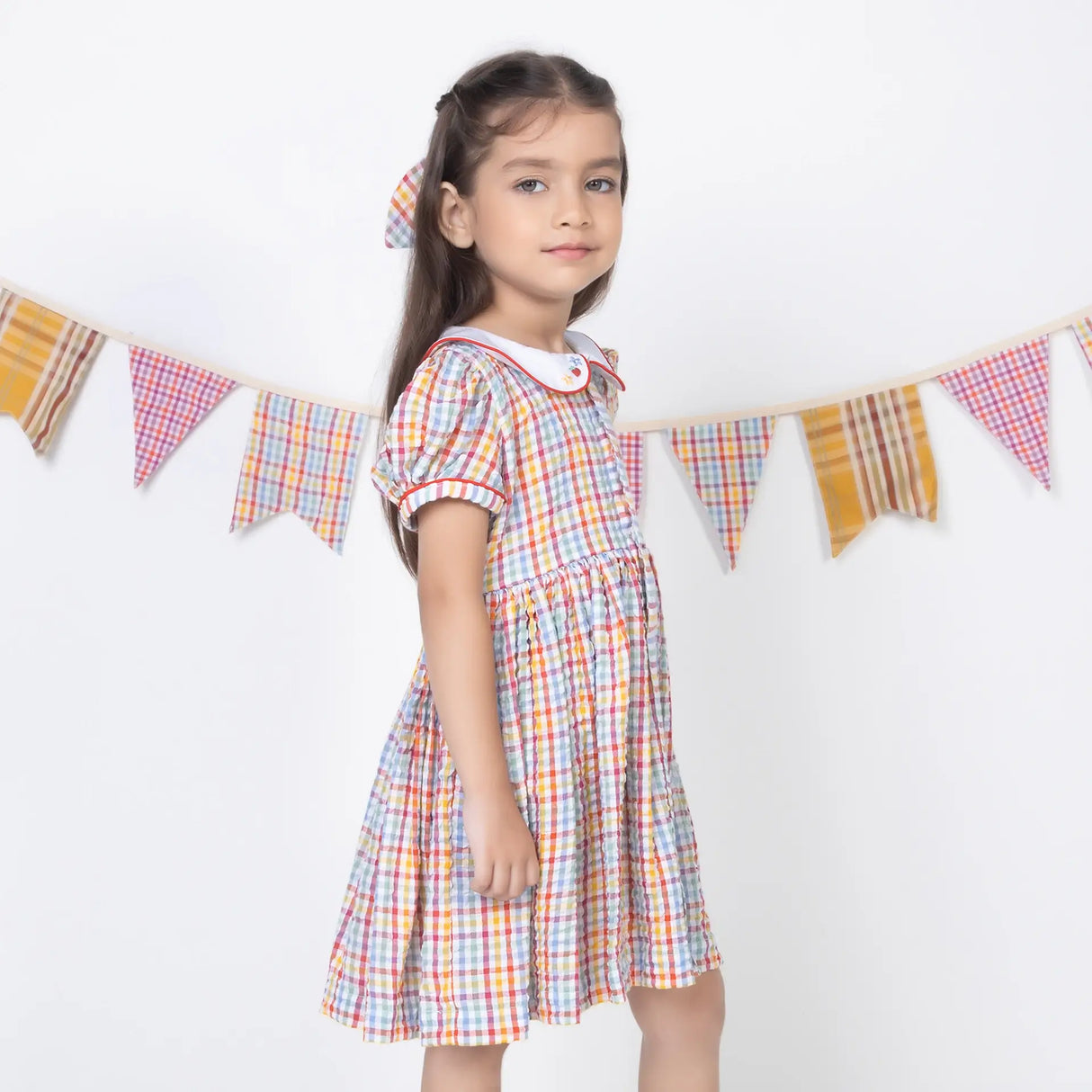 Side pose of a girl in a multi-color checked embroidered cotton puffed sleeves dress.