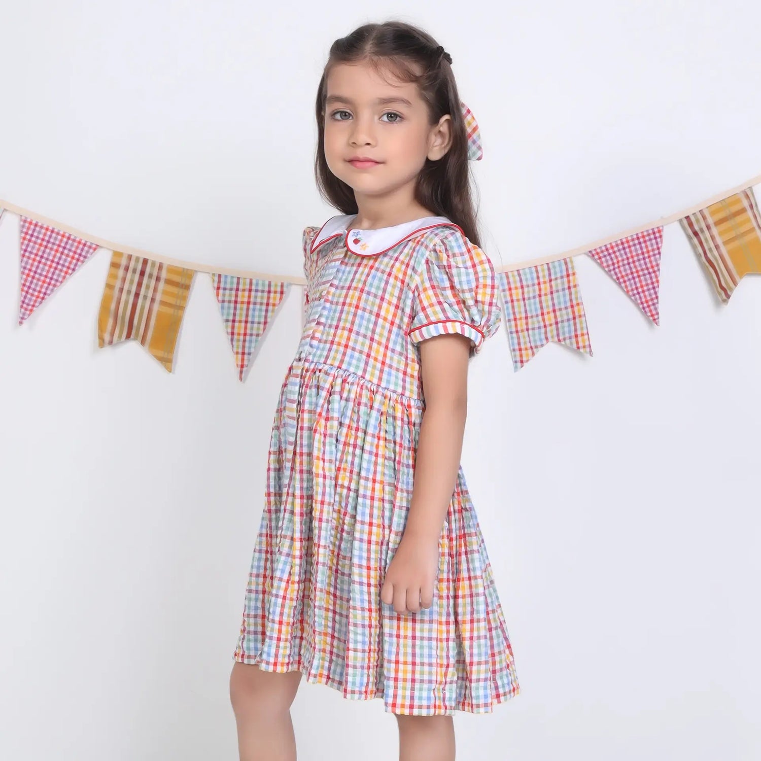 Side pose of a girl in a multi-color checked embroidered cotton puffed sleeves dress.