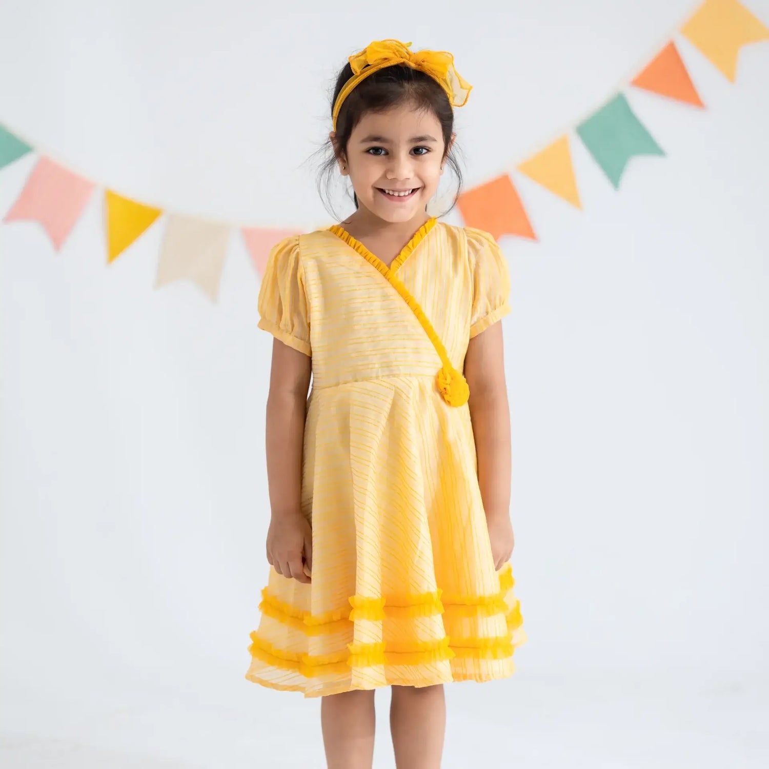 "A girl dressed in a yellow crossover chanderi puffed sleeves dress."