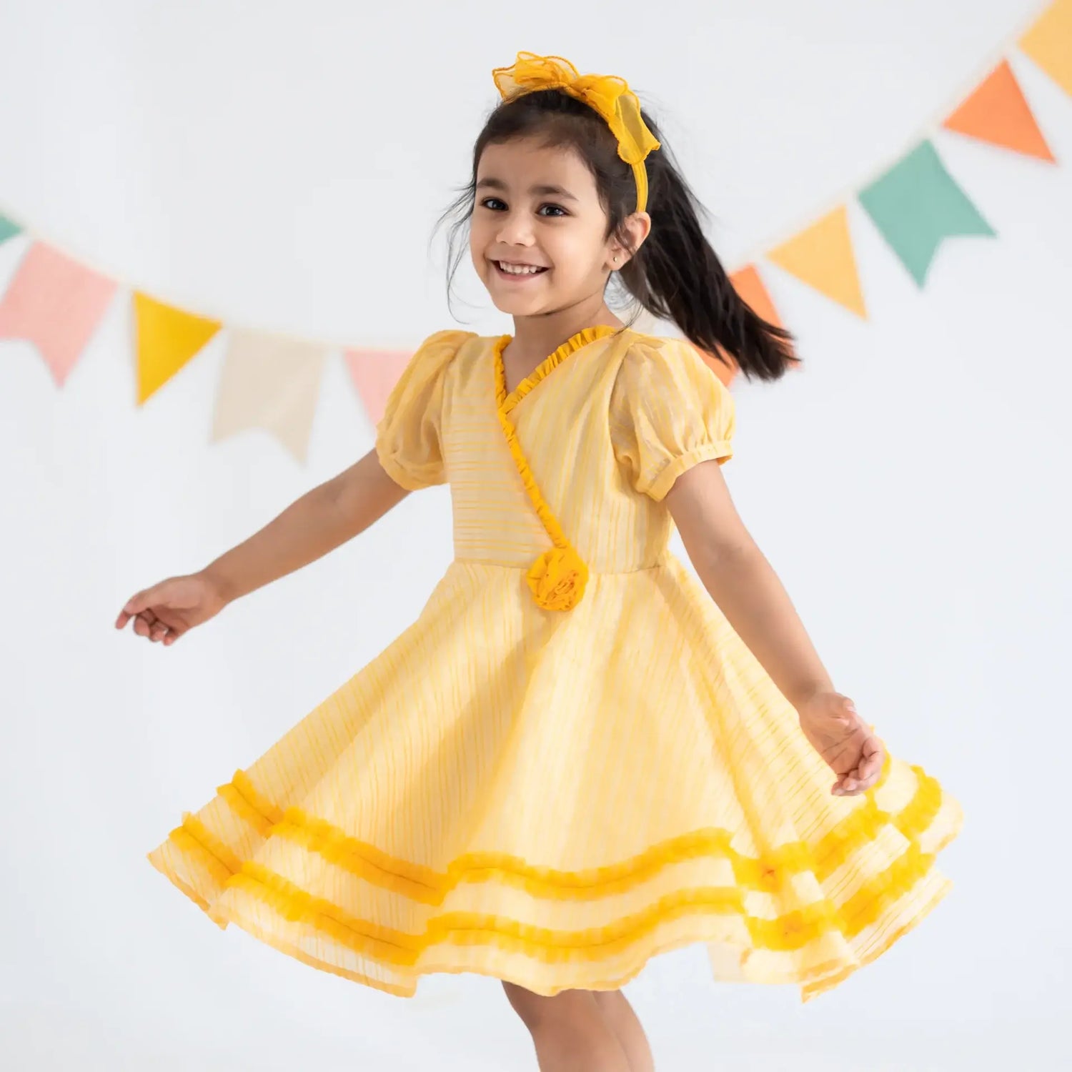"A little girl twirling in a yellow crossover chanderi puffed sleeves dress."