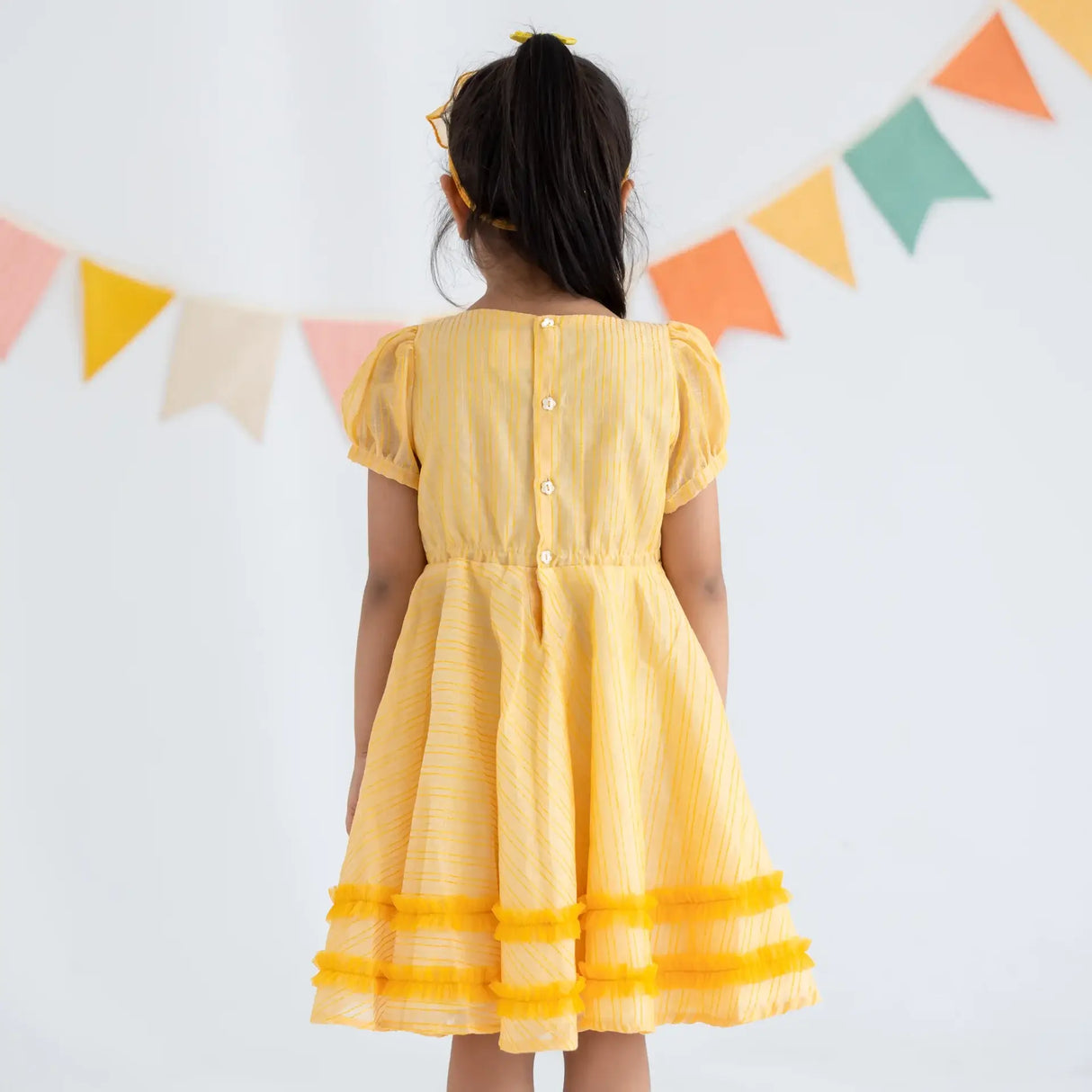 "Back view of a girl in a yellow crossover chanderi puffed sleeves dress."