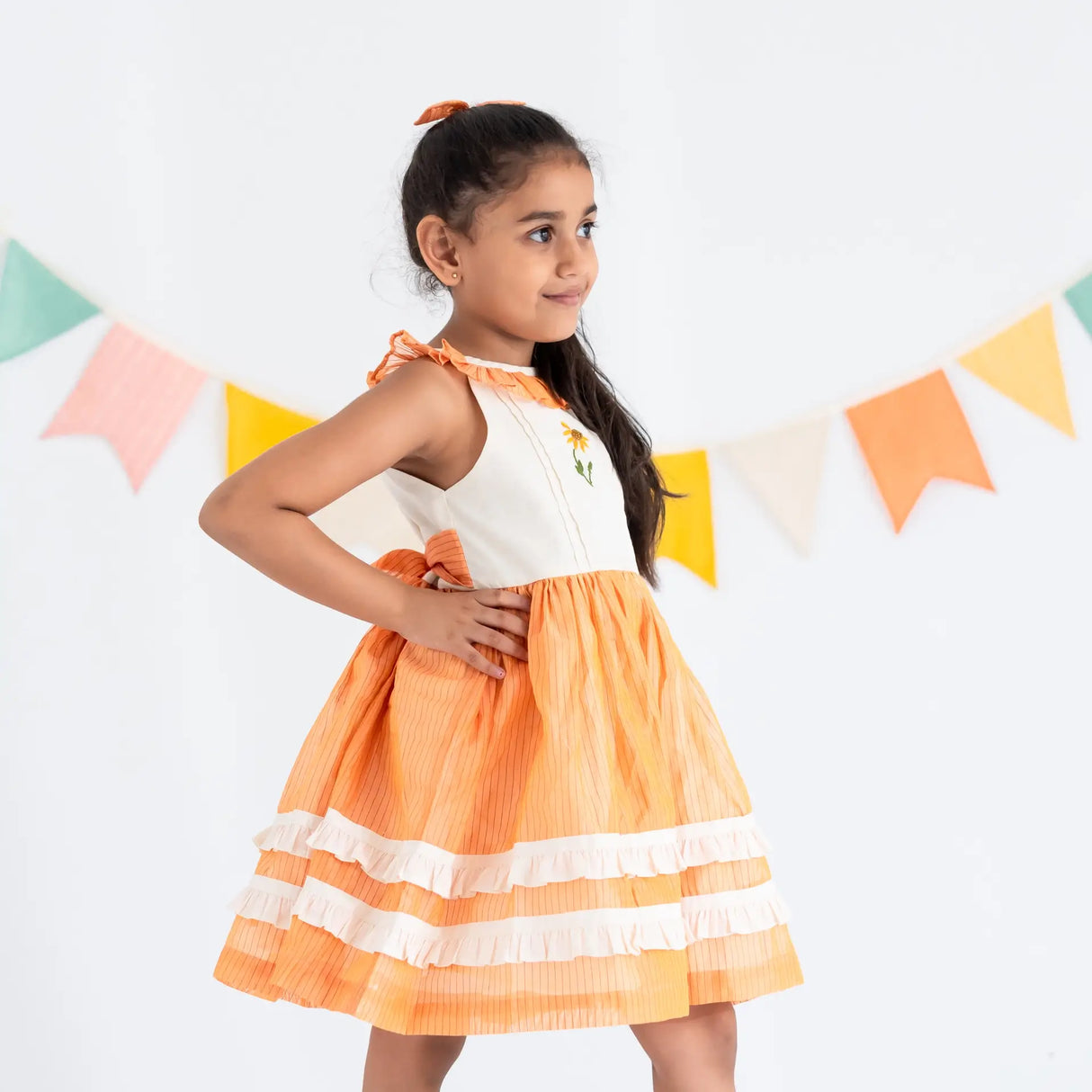 Side view of a girl dressed in an orange hand embroidered zari striped chanderi sleeveless dress.