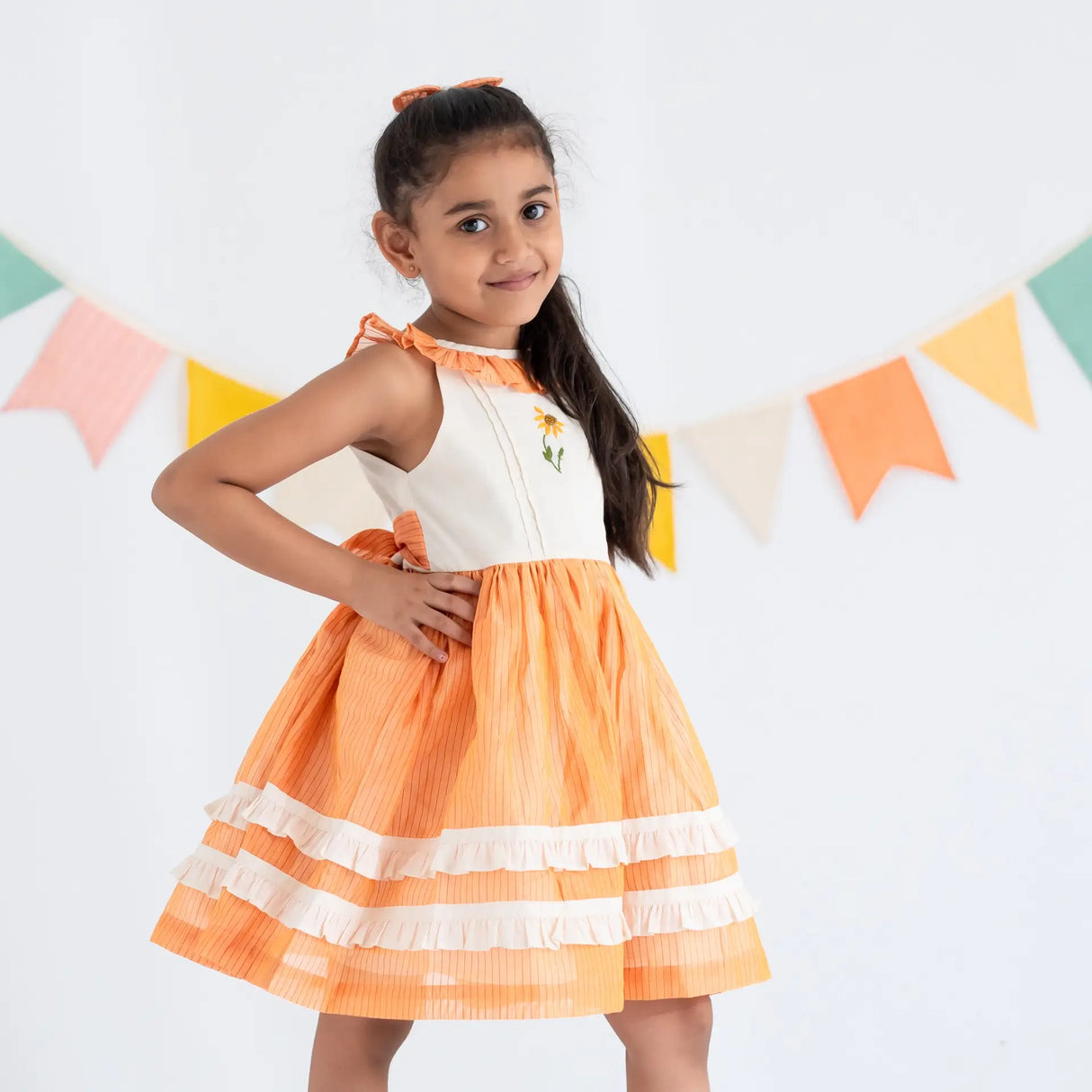 Side view of a girl dressed in an orange hand embroidered zari striped chanderi sleeveless dress.