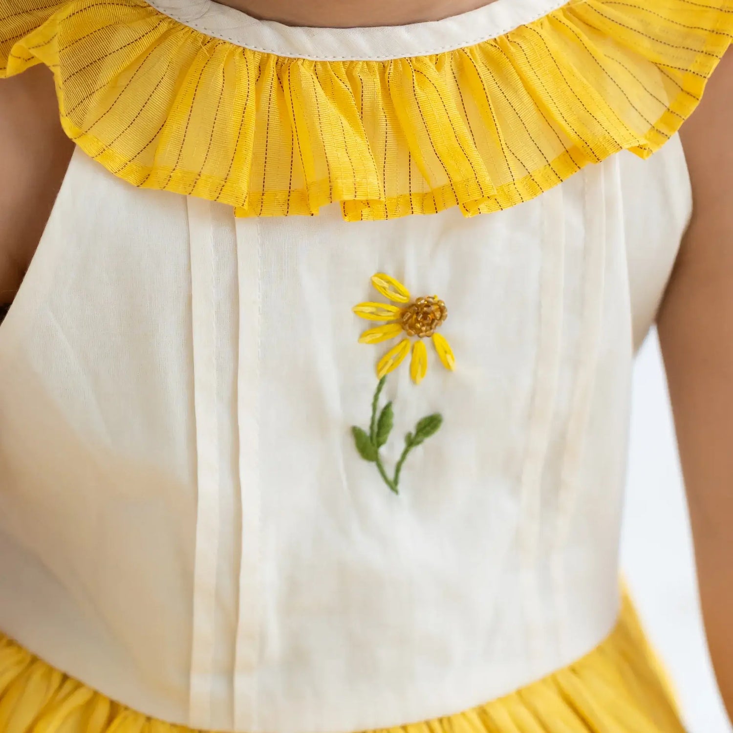 "Close-up of the ruffle neckline and hand embroidery on the yellow hand embroidered zari striped chanderi sleeveless dress."