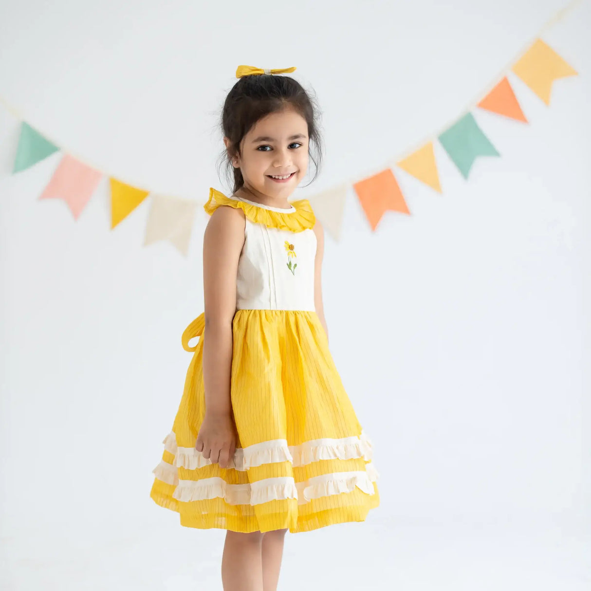 "Side view of a girl dressed in a yellow hand embroidered zari striped chanderi sleeveless dress."