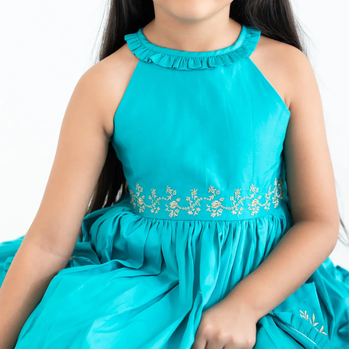 "Close-up of the embroidery and ruffled neck in a teal embroidered cotton satin dress."