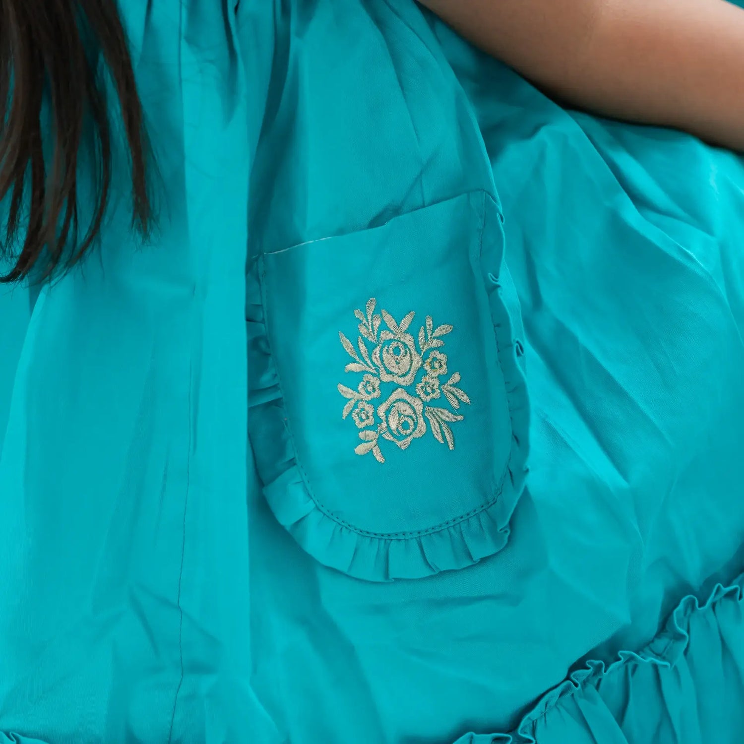 "Close-up of the pocket details in a teal embroidered cotton satin dress."