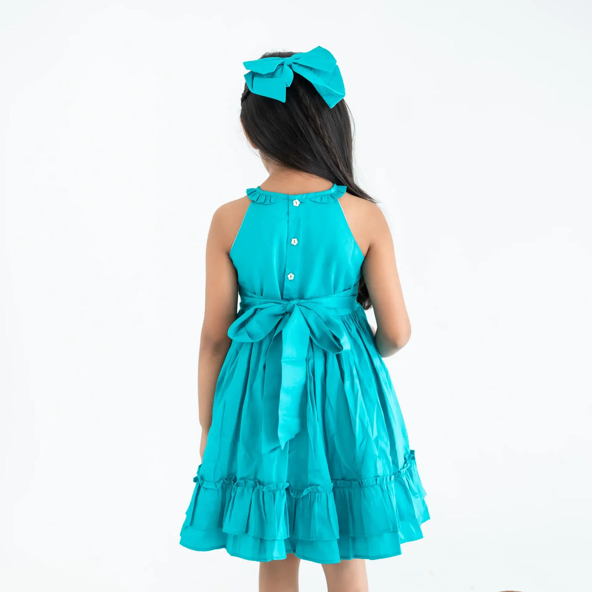 "Back pose of a girl dressed in a teal embroidered cotton satin sleeveless dress with pockets."
