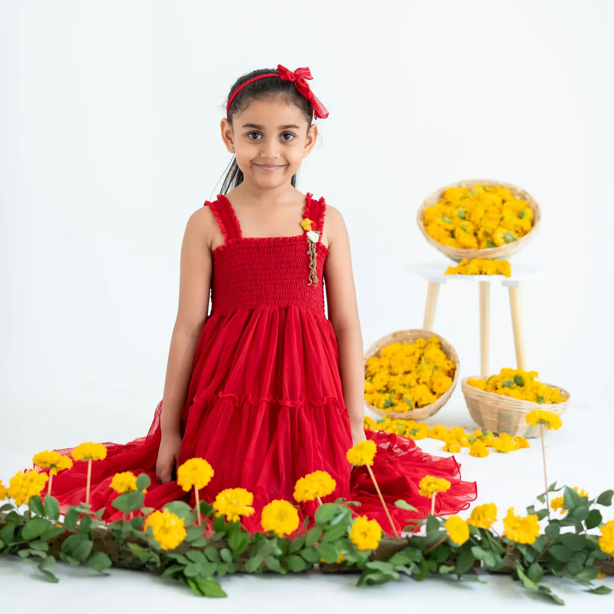A little girl seated, wearing a red hand-embroidered crochet nylon tulle sleeveless dress.