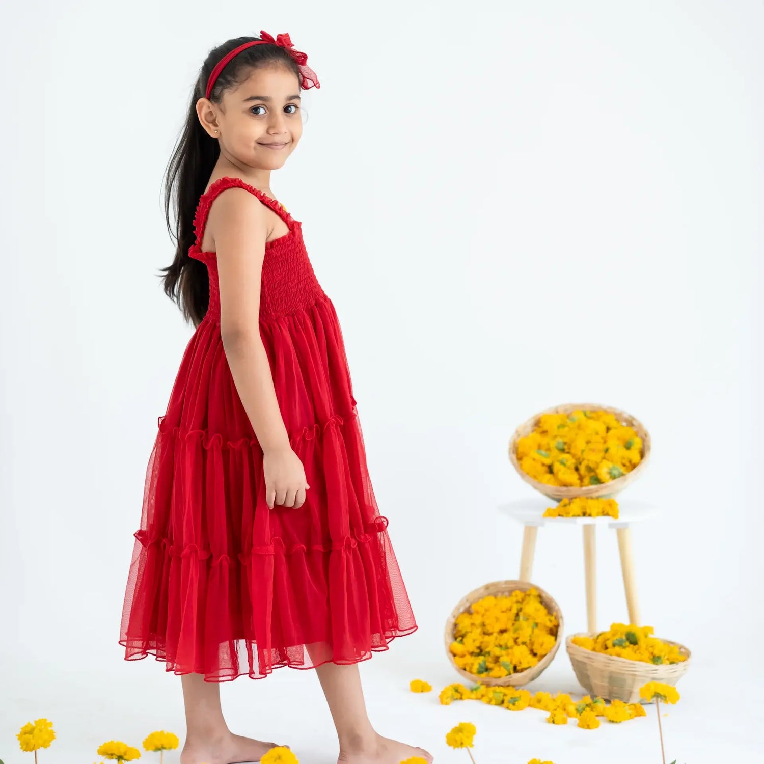 A side pose of a little girl wearing a red hand-embroidered crochet nylon tulle sleeveless dress.
