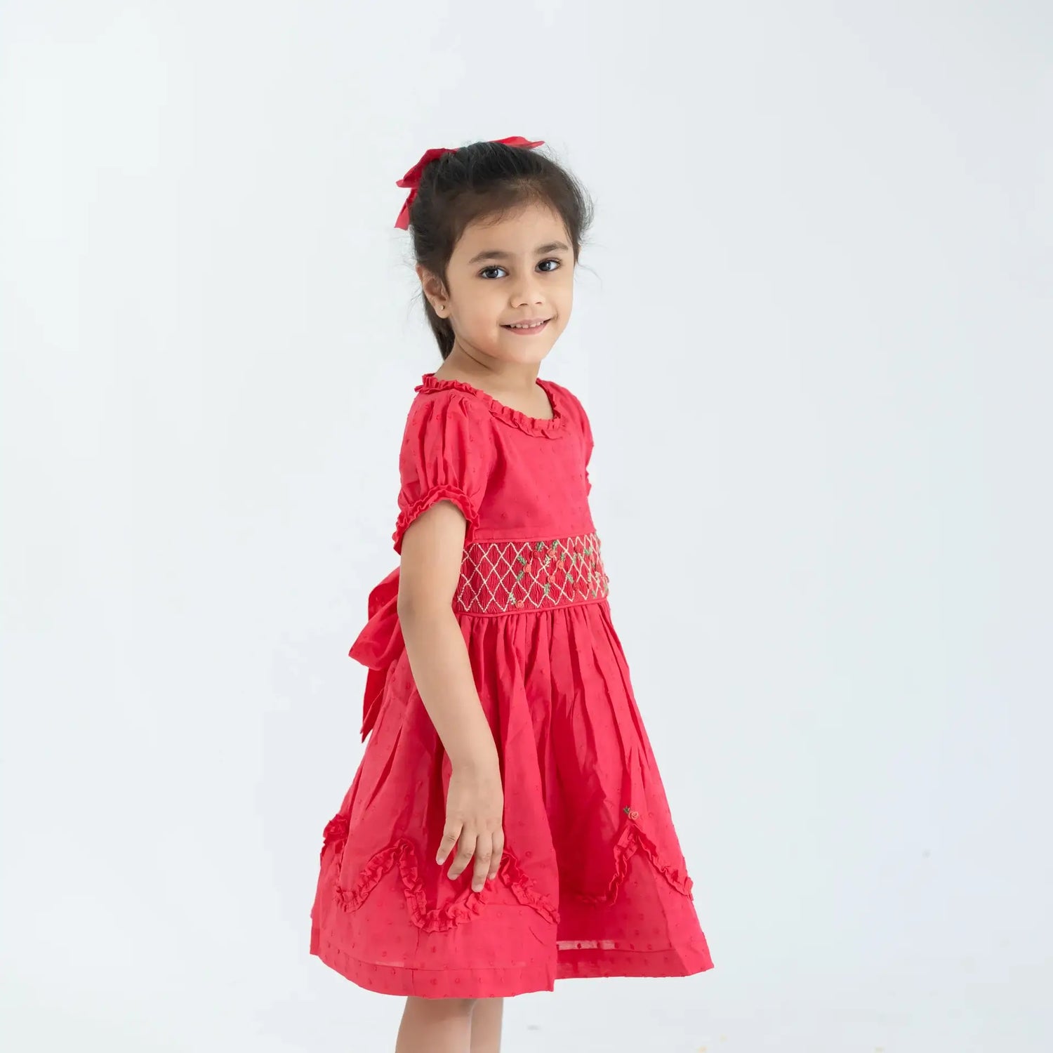 "Side view of a girl in a coral swissdot hand smocked and embroidered cotton puffed sleeves dress."