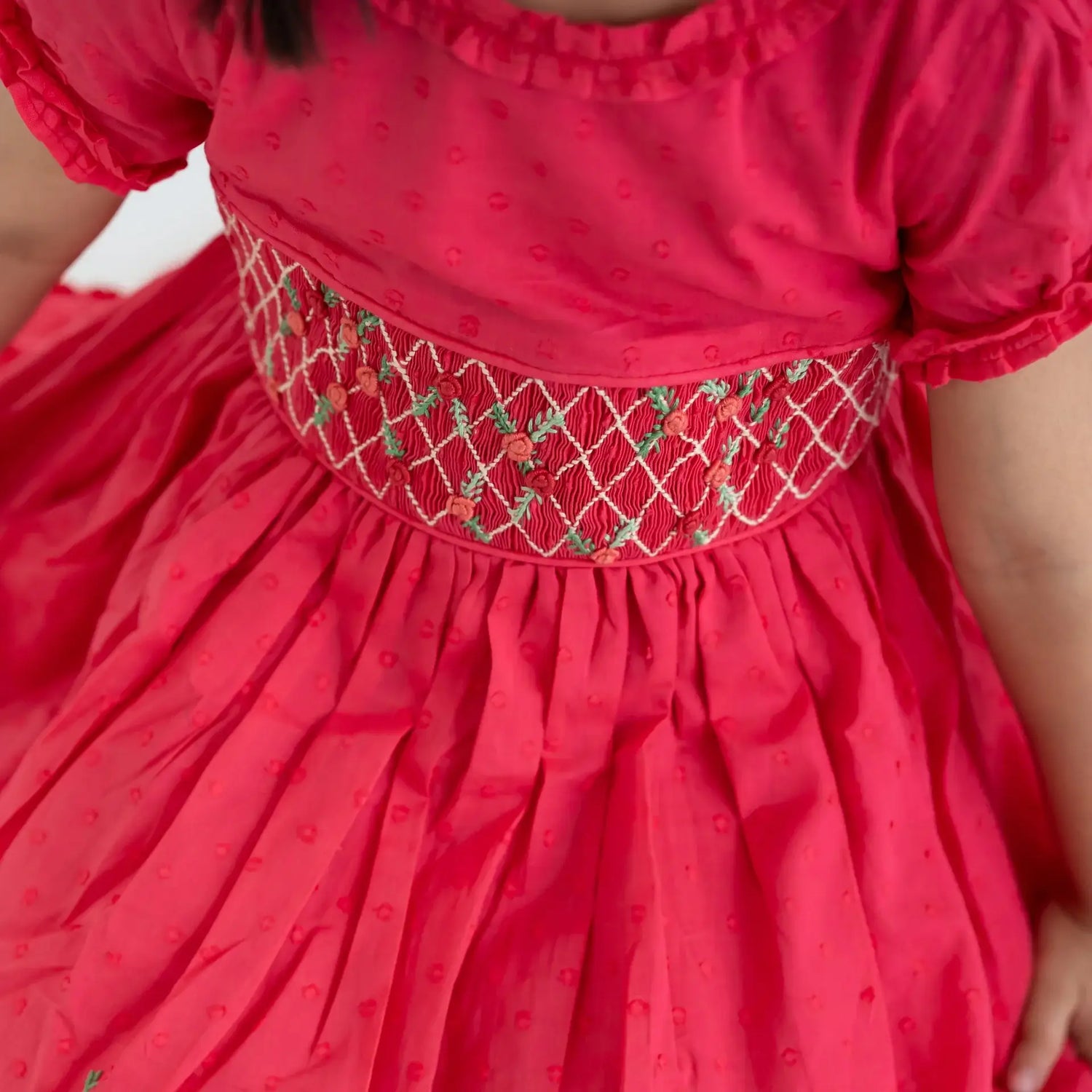 "Close-up of the hand smocking and embroidered details on the coral swissdot hand smocked and embroidered cotton puffed sleeves dress."