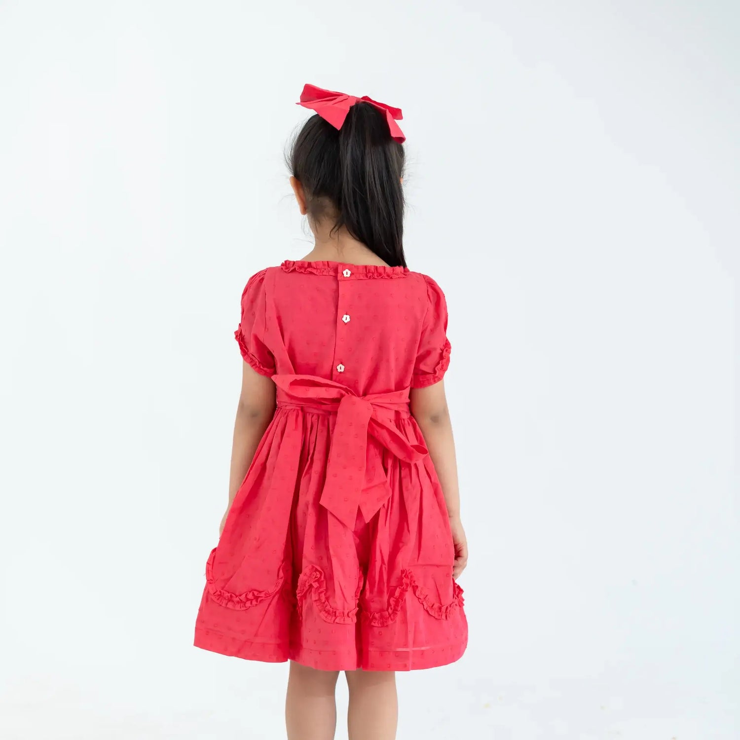 "Back view of a girl dressed in a coral swissdot hand smocked and embroidered cotton puffed sleeves dress."