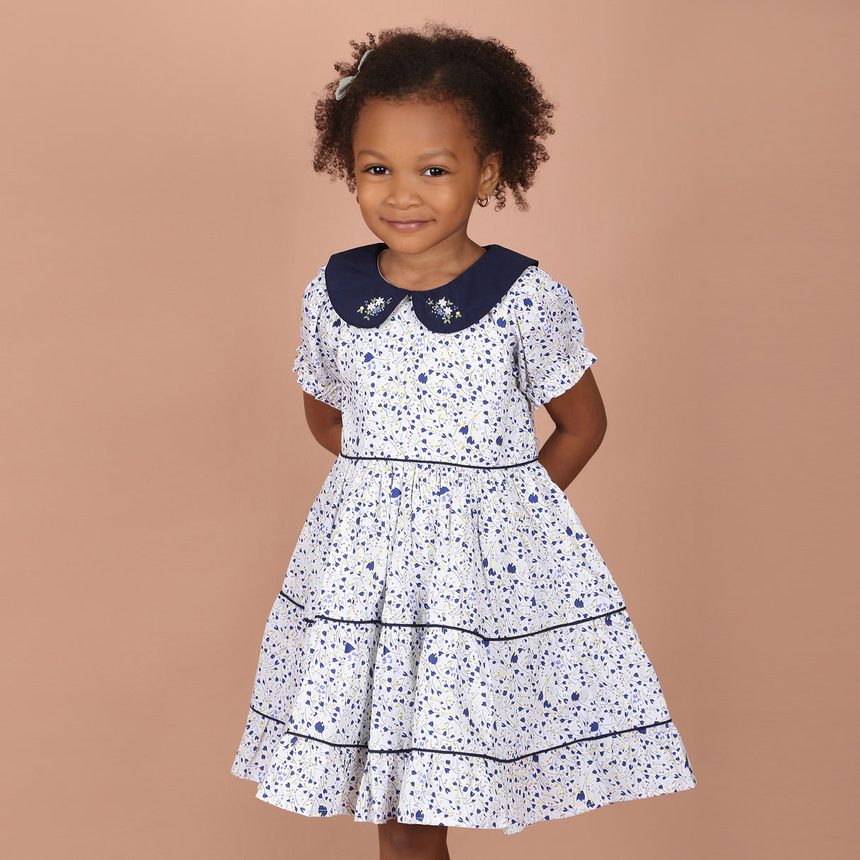 girl wearing white floral hand-embroidered girls dress with navy blue peter pan collar and layered skirt