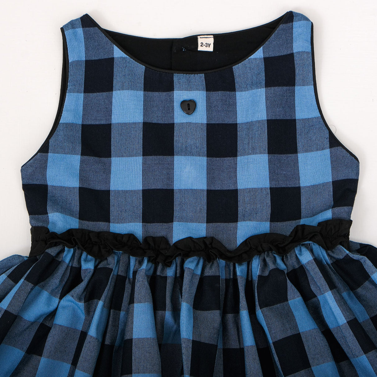 Close-up front view of blue and black check dress with black neckline trim, and decorative front button
