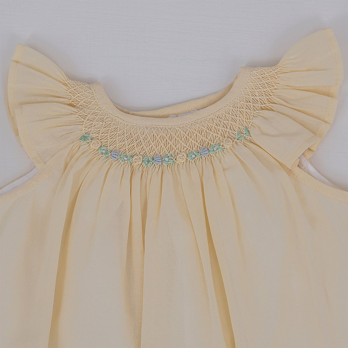 Close-up view of hand smocking and floral embroidery detailing on baby set