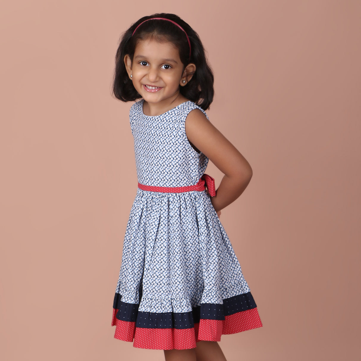 side view of girl in a navy ditsy floral dress with red waistband
