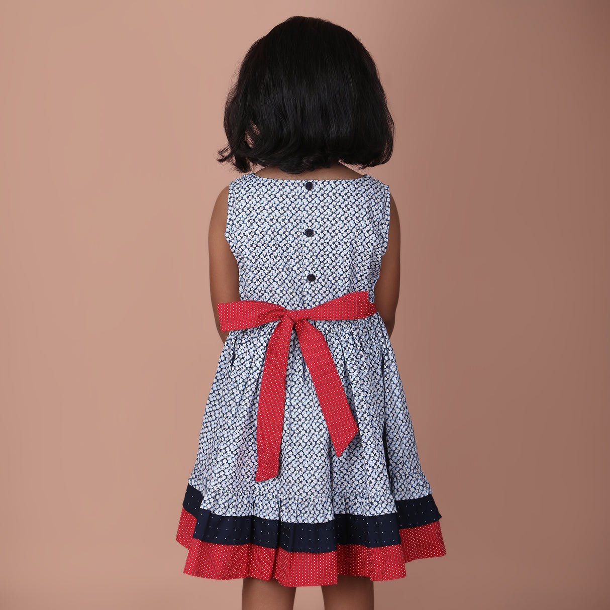 back view of a navy ditsy floral patterned girls dress with red bow tie and button details